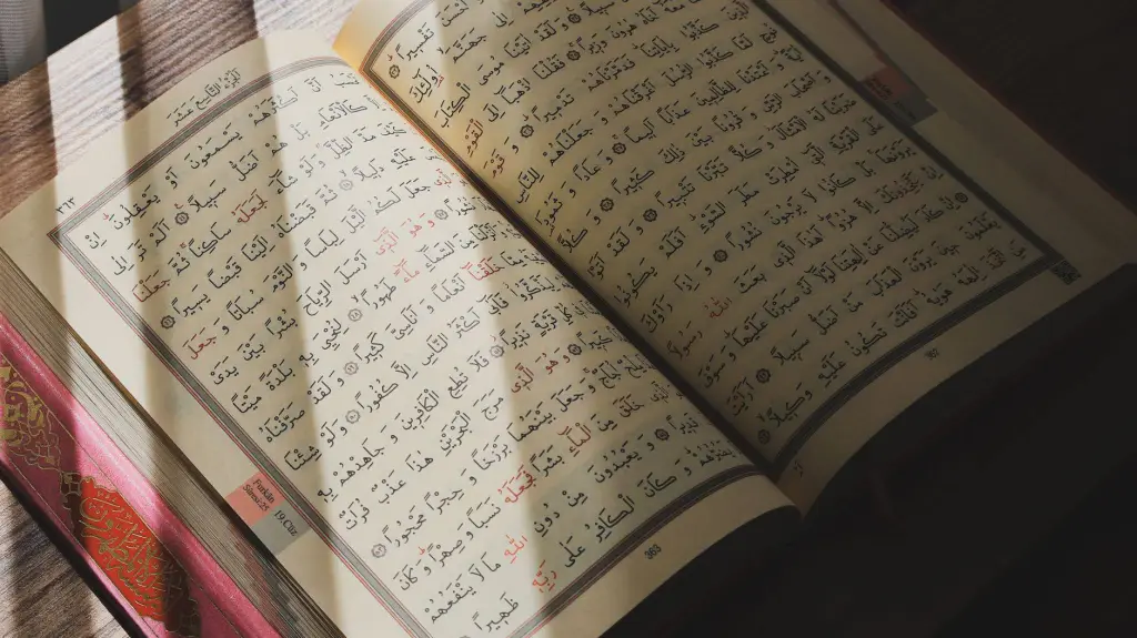 An open Quran with Arabic script illuminated by natural sunlight on a wooden surface.