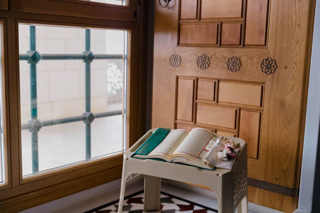 An open Quran on a table by a window in a serene indoor setting, capturing a moment of reflection.