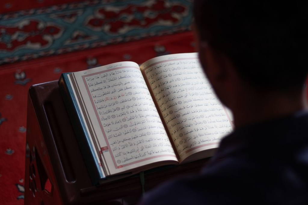 A person reads the Quran inside a mosque with intricate carpet design, reflecting peace and spirituality.