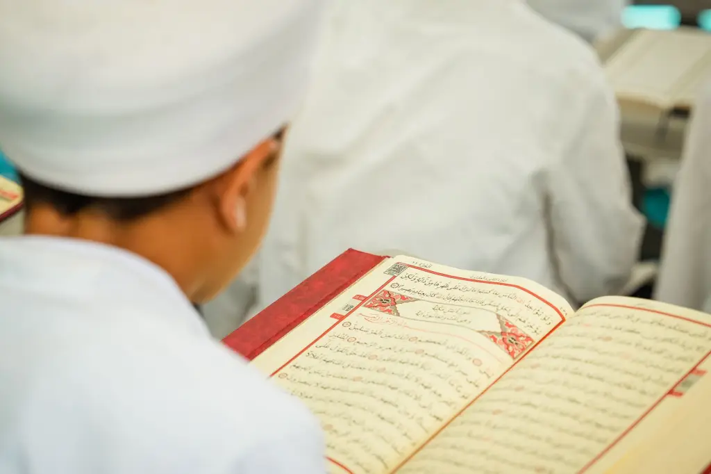 Young student in white attire reading Quran during religious study class.