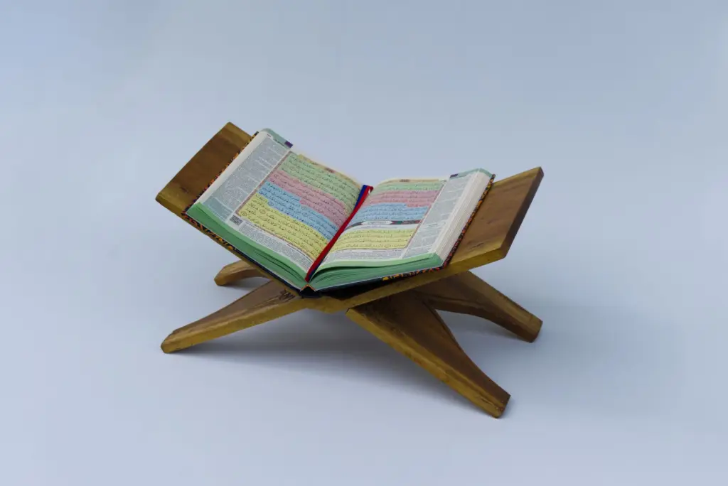 A Quran placed open on a traditional wooden stand, isolated on a neutral background.