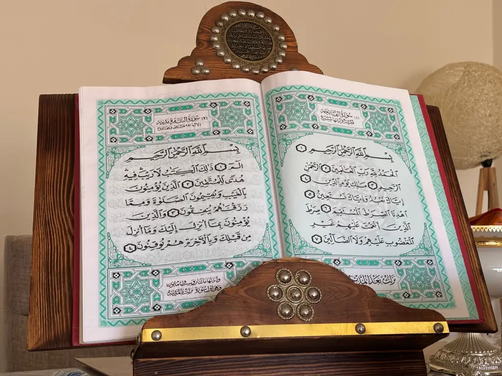An open Quran on a decorative wooden stand in a cozy indoor environment.