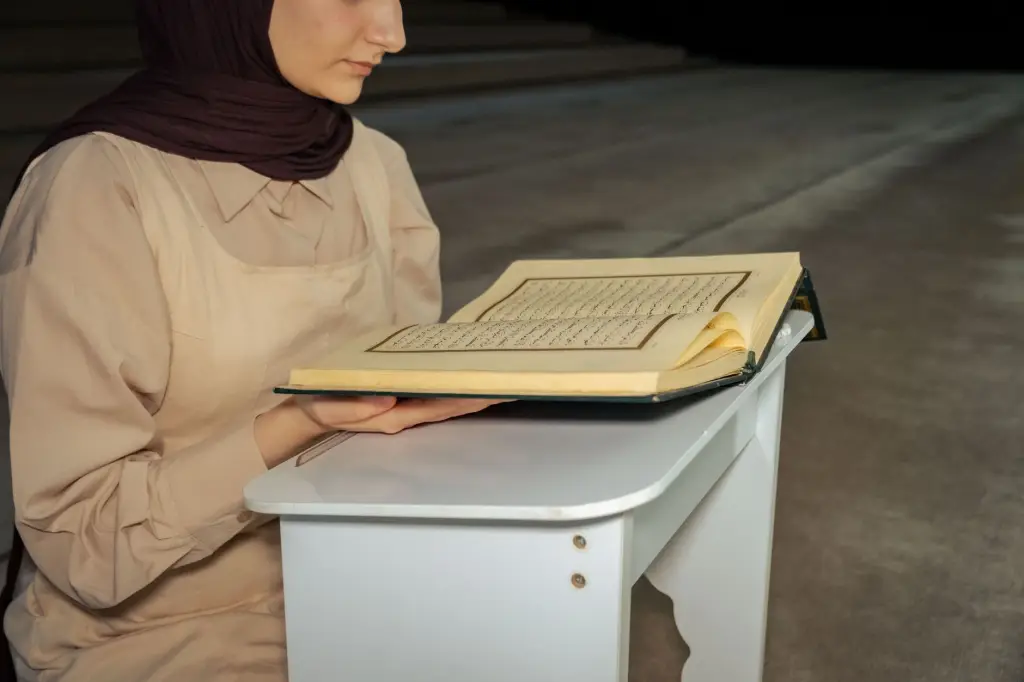 A woman wearing a hijab reads a religious book in a serene indoor setting. Tranquil scene focused on spirituality.