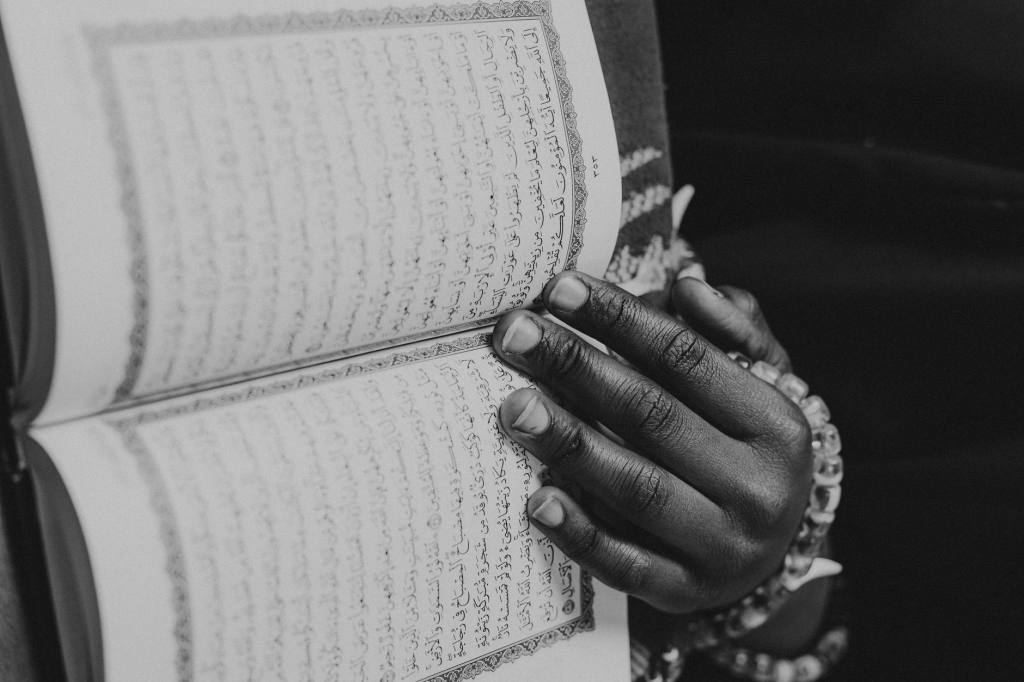 Monochrome image of a hand holding an open Quran, emphasizing spirituality and religious study.