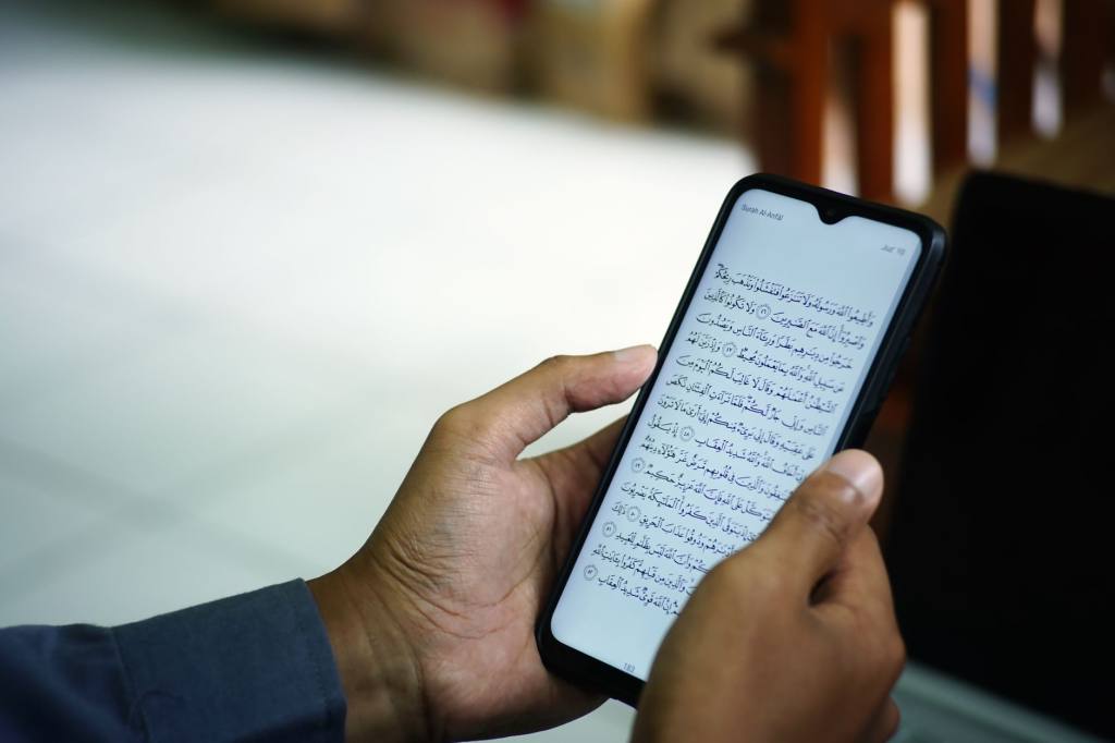 A man reading the Quran on a smartphone inside a mosque, symbolizing modern technology meeting traditional faith.