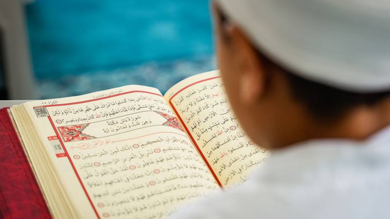 A young child immersed in reading the Quran, highlighting Islamic devotion and education.
